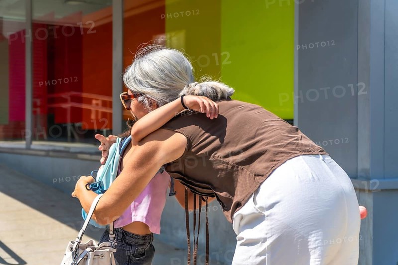 Grandmother embracing her young granddaughter, who is wearing a backpack, sharing a moment of affection and care during a school pickup, reflecting family love and daily routine