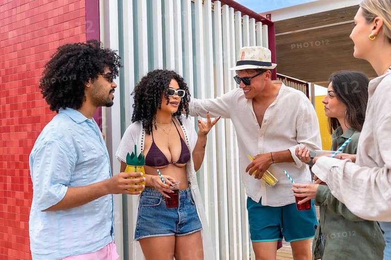 Group of diverse friends is standing outdoors, drinking refreshments and enjoying a cheerful summer hangout, having fun with lively conversation and carefree moments