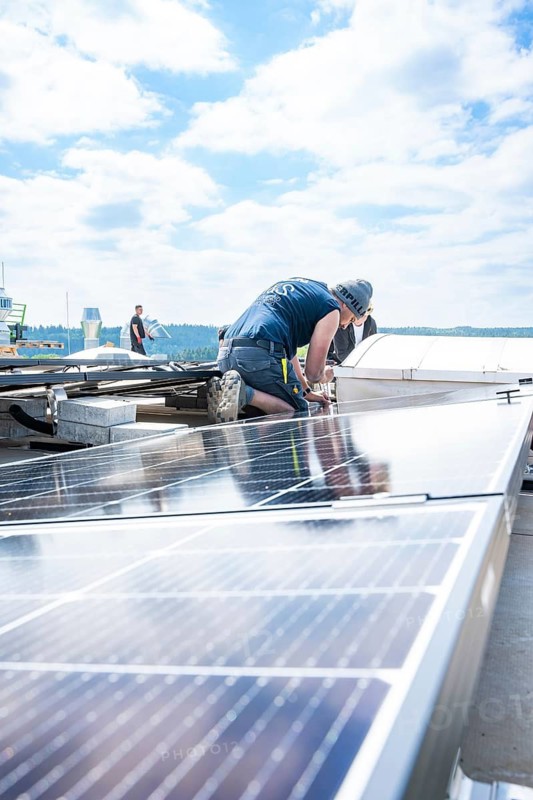 Craftsman working on a roof with solar panels under a blue sky, PV Montage, Perrot company, Calw, Germany