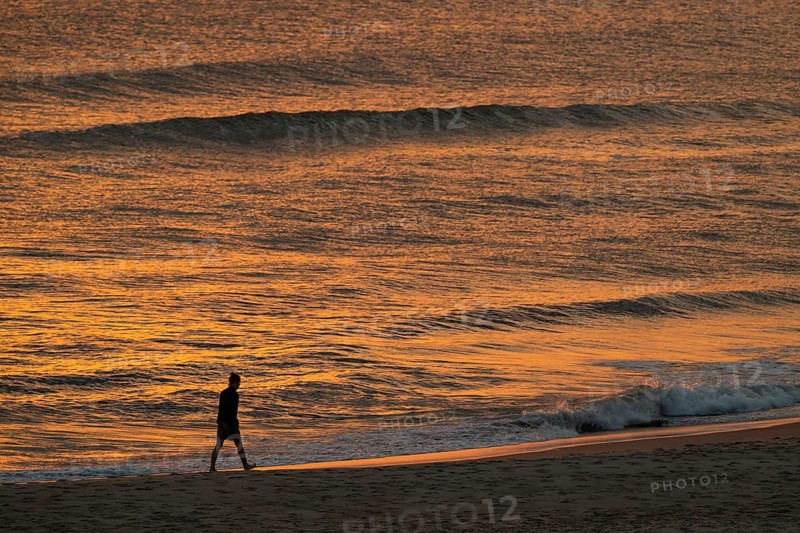 Walkers on the beach, setting sun colors the sea and waves golden, Houvig Beach, North Sea, Denmark
