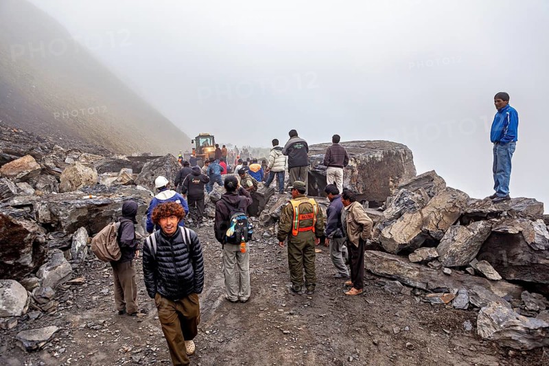 People wearing protective vests watch a foggy construction site, rockslide on the pass road towards Rurrenabaque through the Andes on the Road of Death in Bolivia