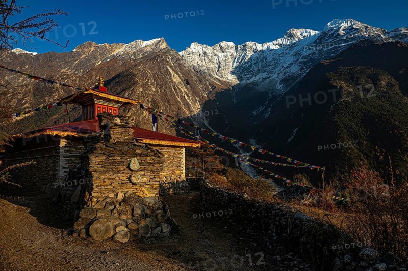 Small Buddhist monastery with manistones in the evening light in front of snow-capped mountains of the Siringi Himal mountain range, Tsum Valley, Himalayas, Nepal