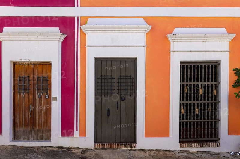 Detailed view of traditional wooden doors and a window with iron grilles on vibrant pink and orange colonial building facades in historic Old San Juan Puerto Rico