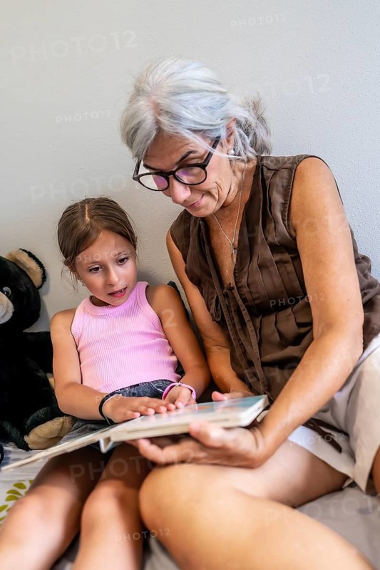 Grandmother and granddaughter bonding while sharing a storybook, fostering love for education and creating happy childhood memories in a household setting
