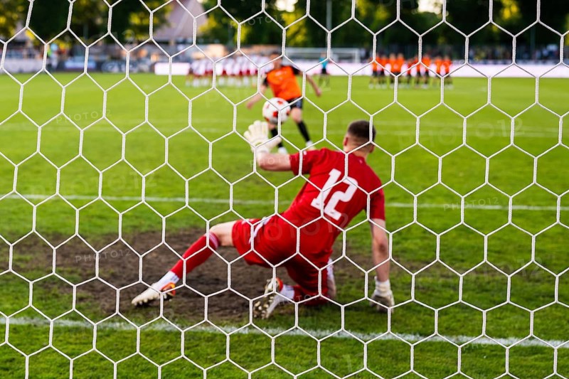 View through the net of a soccer goalkeeper in a red kit preparing to defend a penalty kick during a football match in Glogow, Poland