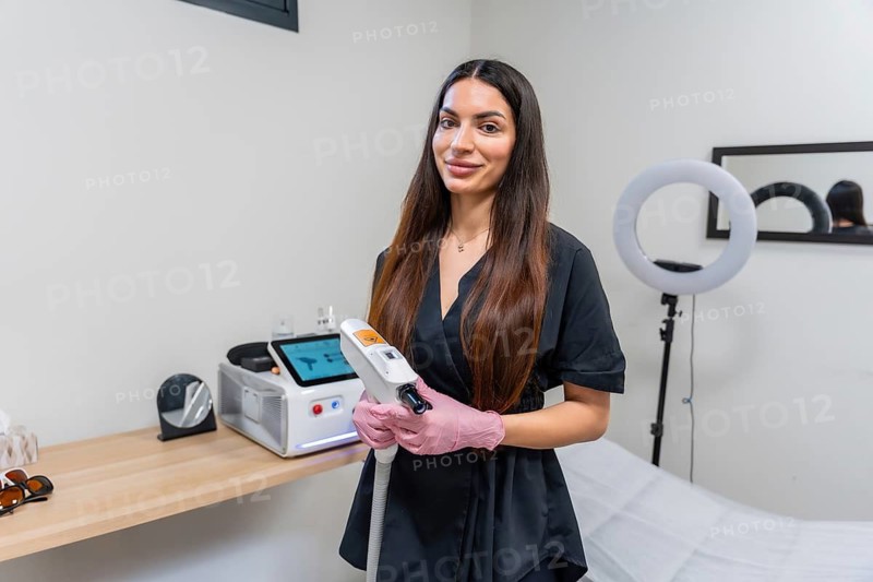 Female aesthetic medicine professional standing in a modern clinic, holding a laser device, and ready to perform skincare procedures like tattoo removal