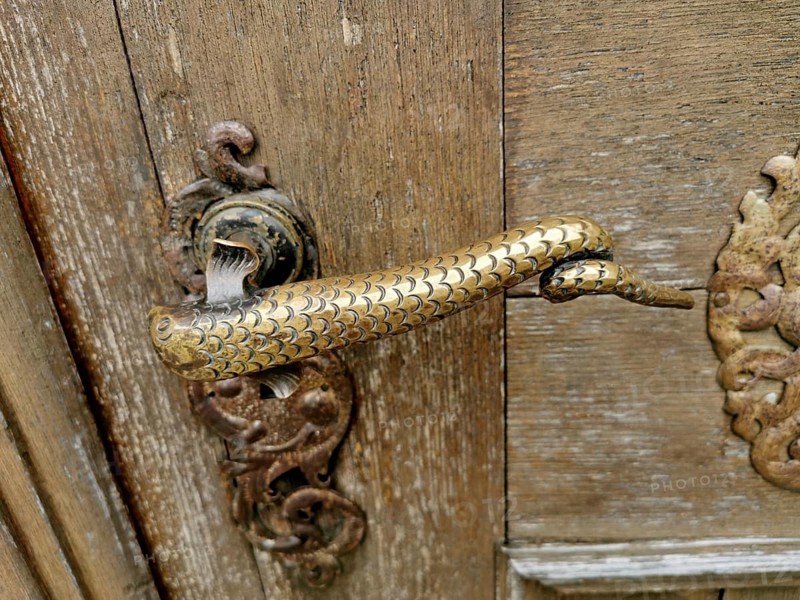 Artfully designed brass or bronze door handle in the shape of a snake or a mythical creature with scale structure at the monastery church, Mönchsdeggingen monastery, former monastery of the Mariannhill Missionaries, near Nördlingen on southern Riesrand, Danube-Ries district, Swabia, Bavaria, Germany