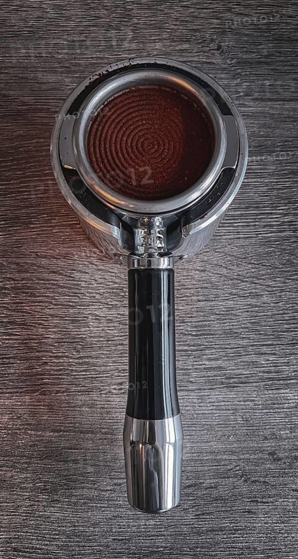 Freshly pressed coffee powder in a portafilter, on a textured wooden table, portafilter of an espresso machine filled with coffee powder