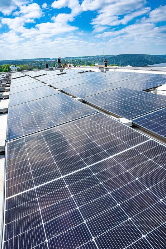 Worker on a large solar system roof in a countryside area, blue sky, PV installation, Perrot company, Calw, Germany