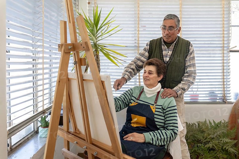 Senior couple standing together and looking at a canvas on an easel in a bright home art studio