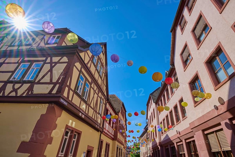 Sunbeams flood a street with half-timbered houses and colorful lanterns, Lohr am Main, Schneewittchenstadt, Main-Spessart district, Spessart, Mainfranken, Lower Franconia, Bavaria, Germany
