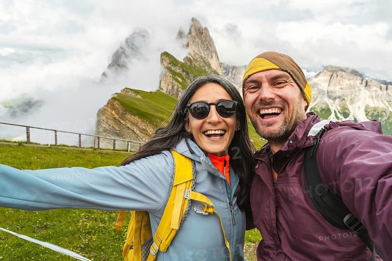 Cheerful couple of hikers friends taking selfie in Dolomites mountains.Millennial guy girl enjoying summertime day out trip laughing at camera together - Millennial travelers standing in scenic nature