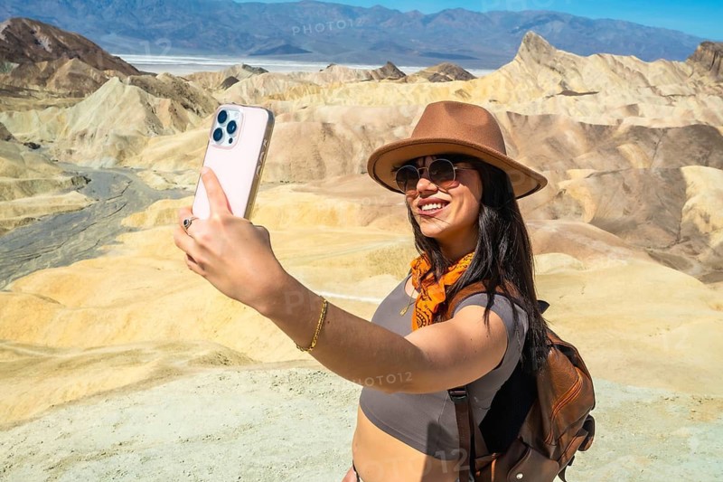 Happy woman taking a selfie with phone, documenting her travel memories while exploring the unique badlands and vast desert landscape of death valley national park
