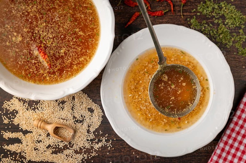 Quinoa soup is poured into a plate surrounded by spices and red hot peppers
