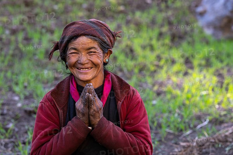 Portrait, elderly friendly smiling Nepalese woman, local of the Tsumba Tibetan ethnic group folding her hands in greeting Namaste, Tsum Valley, Himalayas, Nepal