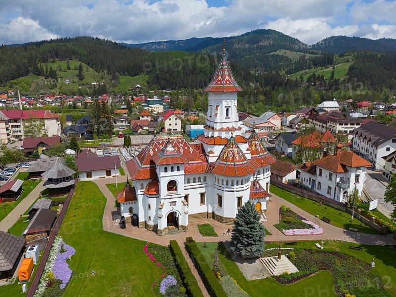 A picturesque Orthodox church with a red-decorated roof in the midst of a green mountainous village landscape, aerial view, Assumption of the Blessed Virgin Orthodox Church, Câmpulung Moldovenesc, Kimpolung, Suceava County, Bukovina Region, Romania