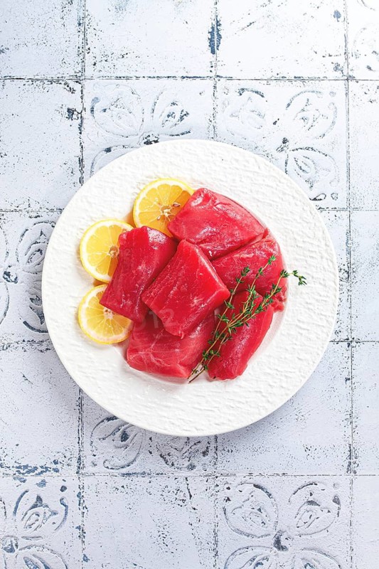 Fresh tuna slices, on a white plate, with lemon slices and herbs, top view, no people