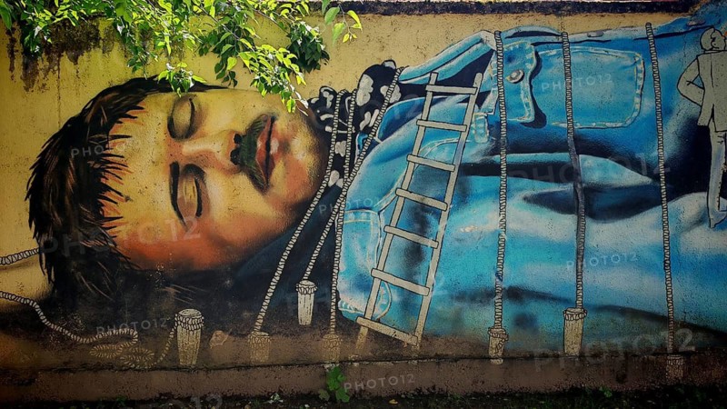 A mural depicts Guliver a man in a blue robe with ropes in a natural setting, Zagreb, Croatia