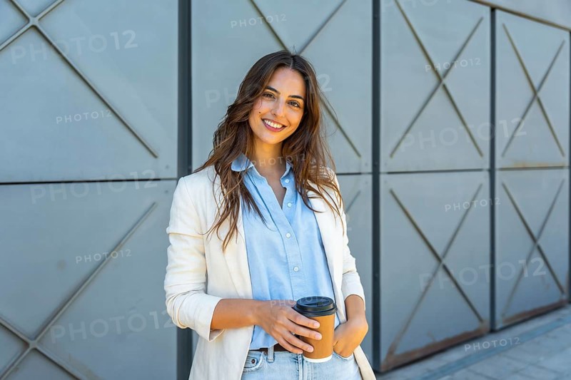 Confident young professional woman in a light blazer smiling outdoors, holding a reusable coffee cup relaxed entrepreneur vibe, modern urban business lifestyle and success