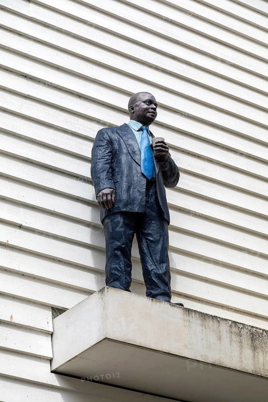 Man with Cup artwork painted bronze sculpture by Sean Henry 2017 black male standing on ledge, Colchester, Essex, England, UK