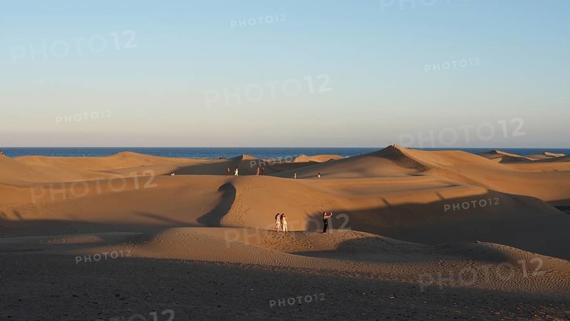 Shadows of a sunset cover the dune landscape with people in front of the vast sea, dunes of Maspalomas, Gran Canaria, Spain