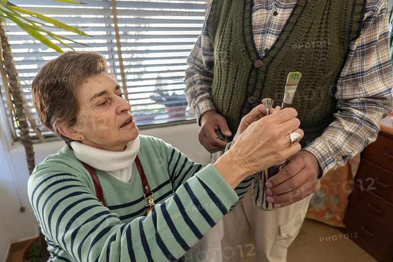 Close-up view of a senior woman selecting a paintbrush from a container while preparing to paint in her home art studio