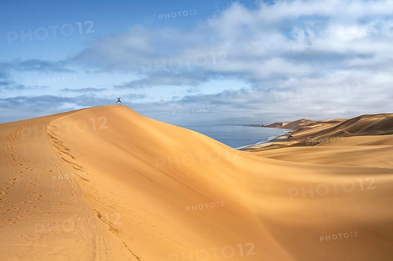 Lonely person jumping on a dune, sand dunes and sea in morning light, Atlantic coast and sandy desert with sea of dunes, Sandwich Harbour, Namib Naukluft Park, Namib Desert, Namibia