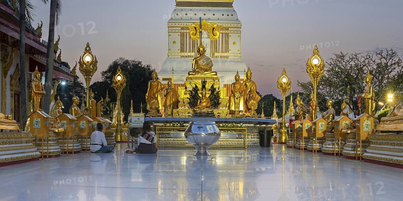 Altar with Buddha statues in front of the chedi decorated with golden ornaments in Wat Phra That Phanom at sunset, temple complex in Amphoe That Phanom, Nakhon Phanom Province, Isan, Thailand