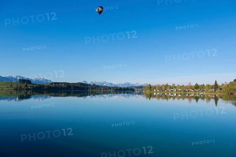 A hot air balloon floats over a lake with mountains in the background in a clear atmosphere, Lech Reservoir, Hochplatte with Ammergebirge, Tegelberg, Säuling and Thannheimer Alps, near Urspring, Upper Bavaria, Bavarian Swabia, Bavaria, Germany
