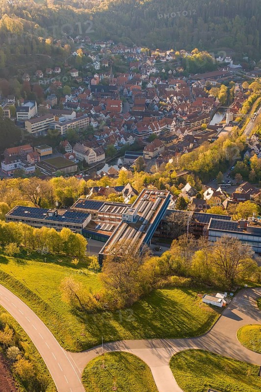 Aerial view of a settlement with traditional houses surrounded by green hills and sunlight, Calw District Office, Calw District, Germany