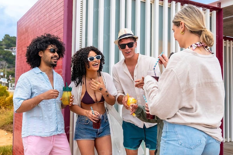 Young friends enjoying sunny beach vacation, laughing and sipping colorful cocktails together, relaxed and cheerful as they celebrate friendship, summer fun and warm days
