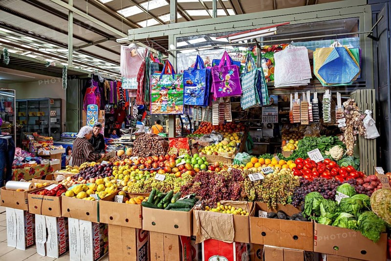 Covered stand with a variety of fruits and vegetables and colorful shopping bags, The Calama market hall in Chile