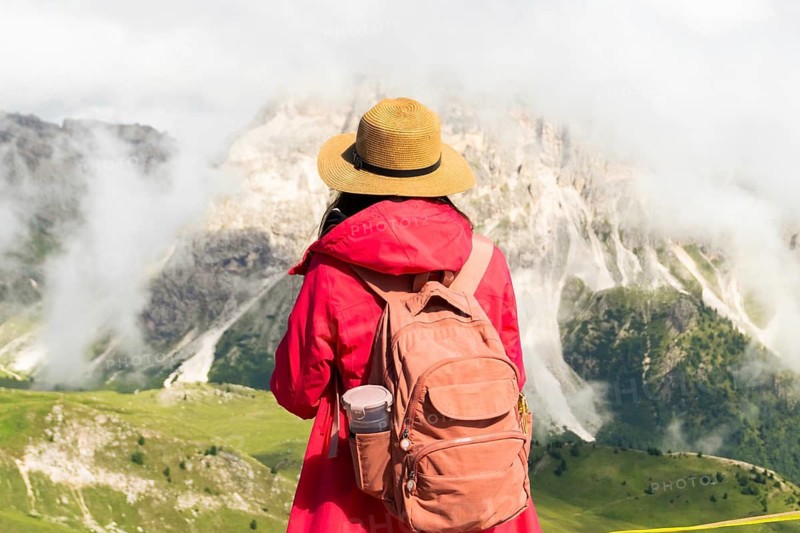 Close up asian female hiker with backpack and straw hat looking at misty mountain peaks deep valley scenic destination Seceda Dolomites South Tyrol Italy. Inspirational ad banner