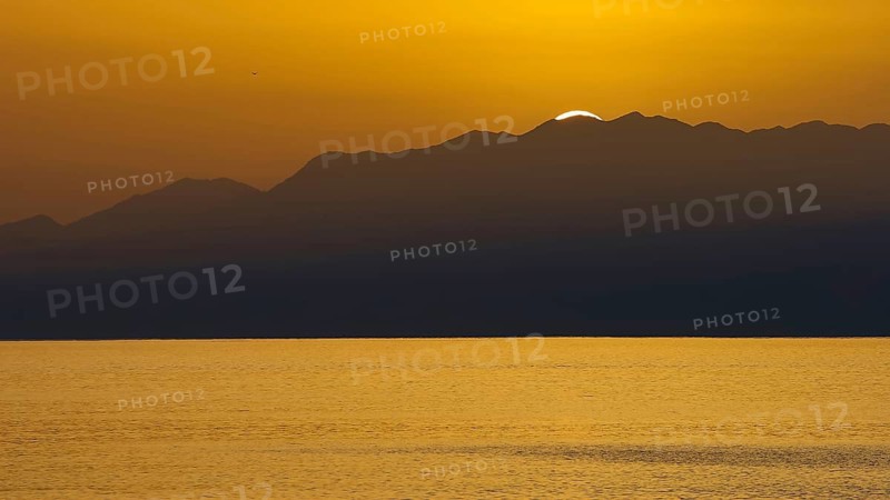 Sunset over sea surface with mountain silhouette in background, Matala, South Coast, Crete, Greek Islands, Greece