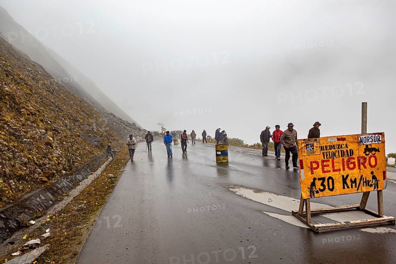People on a wet fog road, warning road sign for car drivers, rockslide on the pass road towards Rurrenabaque through the Andes on the road of death in Bolivia