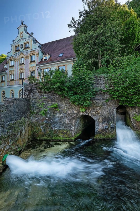 Water flowing from historic stone channels at the Brenzursprung karst spring, with a baroque town house in the background. Koenigsbronn, Baden-Wuerttemberg, Germany