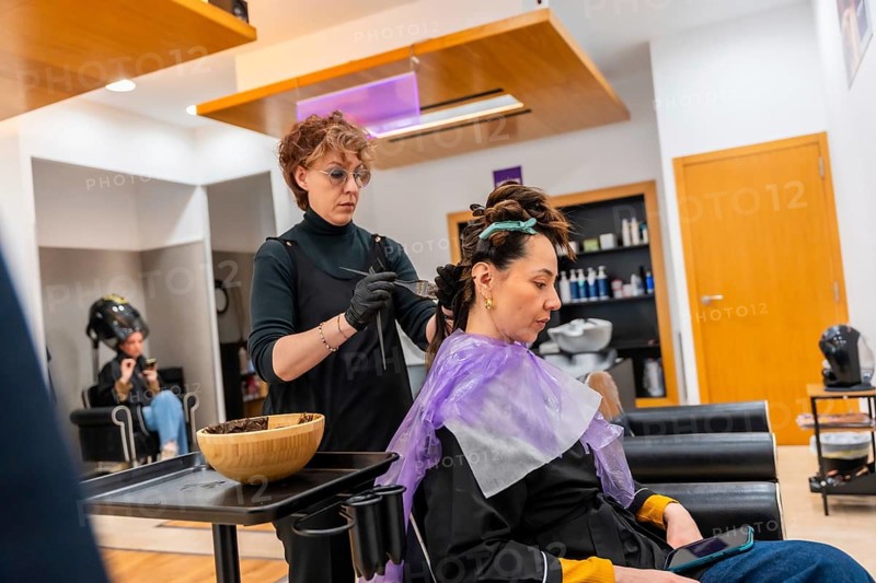 Professional hair stylist wearing gloves and apron carefully applying hair color to a female client's hair during a hair treatment appointment in a modern beauty salon