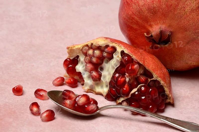 Opened pomegranate and pomegranate seeds in a spoon, Punica granatum