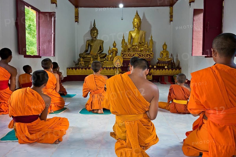 Laotian novices in orange robes in front of a golden Buddha figure in a newly built Buddhist monastery in the village of Muang Ngoi on the Nam Ou River, Phongsali Province, Laos