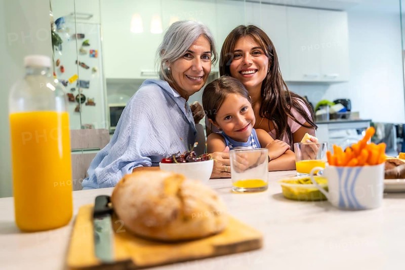 Grandmother, mother, and granddaughter are enjoying a cheerful breakfast together at home, sharing a happy moment around the kitchen table creating lasting family memories