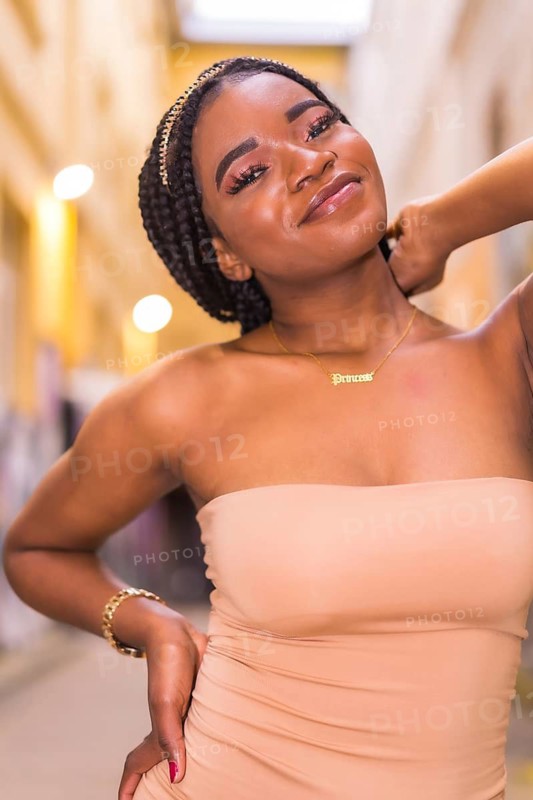 Trendy urban style with a black African girl in a cream colored dress on a city street. Portrait of young woman looking and smiling