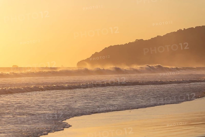 The low sun's golden light illuminates the ocean spray on Carate Beach, with views of Corcovado NP at sunset. Costa Rica