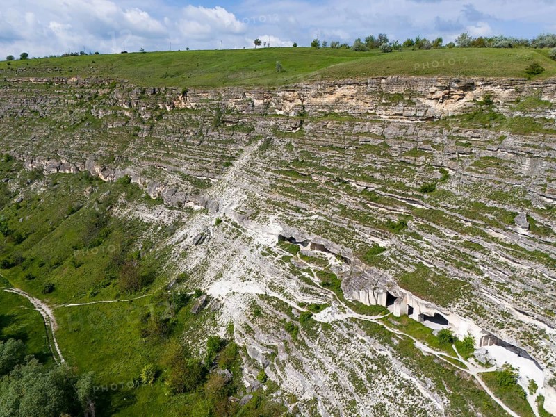 Limestone cliffs with caves and grass on a steep wall under blue sky, aerial view, cave dwellings, FLALT-orhei, Orheiul Vechi, archaeological site, protected landscape area, Orhei district, Republic of Moldova, Moldova