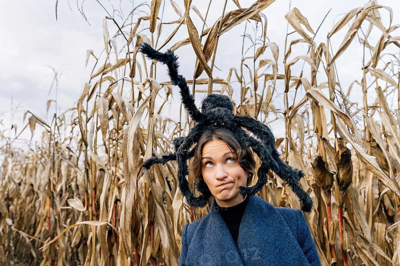 A woman with a distorted face and a toy of a furry large spider on her head. Concept of decorations for the celebration of Halloween