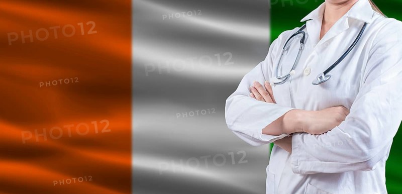Doctor with crossed arms on Ivory Coast flag. Ivorian health and care concept. Female doctor on Ivory Coast flag