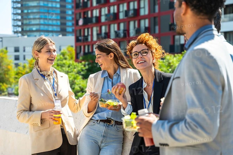 Cheerful business people standing together outdoors enjoying a healthy conversation and lunch, reflecting positivity, teamwork, and a pleasant work environment during their break