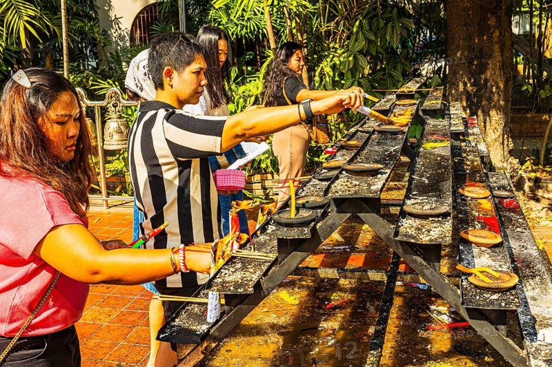 Young Thai and Thai women light incense in the Wat Phra Singh Buddhist temple complex, Chiang Mai Old City Center, Chiang Mai Province, Thailand