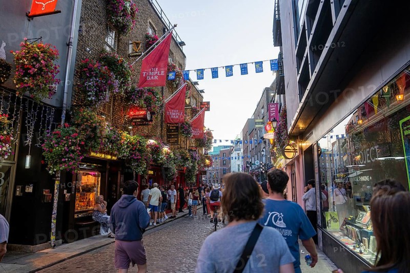 Tourists stroll down a paved street illuminated by shops in the evening, Dublin, Ireland