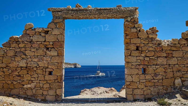 A stone arch with a view of a sailboat on the sea under clear blue sky, Palio Ergostasio Kaolini, Old Kaolin Loading Station, Ruins, Firopotamos, Fishing Village, North Coast, Beach, North Coast, Milos, Cyclades, Greek Islands, Greece