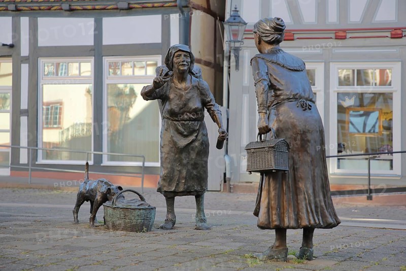 Market Women sculpture by Ewald Rumpf 2009, modern art, bronze sculpture, life-size, two standing woman with index finger, gesture, arm up, gossip, wicker basket, listening, telling, communication, dog figure on shopping basket, market square, Rotenburg an der Fulda, Hesse, Germany